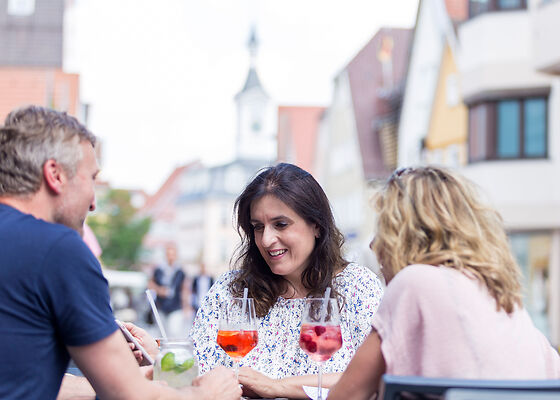 Drei Personen sitzen mit einem Getränk an einem Tisch in der Innenstadt von Aalen