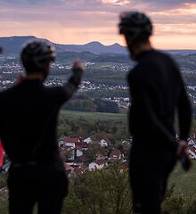 Drei RadfahrerInnen stehen mit dem Rücken zur Kamera und blicken über das Tal